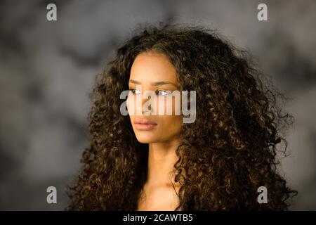 Headshot of a beautiful thoughtful black girl with long curly hair looking off to the side with a pensive serious expression Stock Photo
