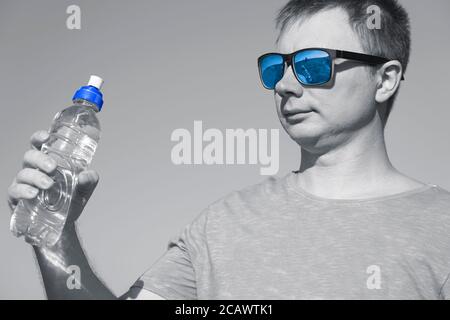 a guy with glasses and a t-shirt holds a plastic water bottle in his hands