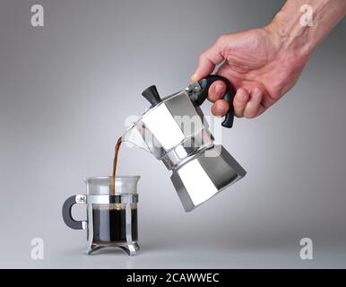 Man's hand holding and pouring italian coffee into a Glass cup. There is path for isolated on white Stock Photo