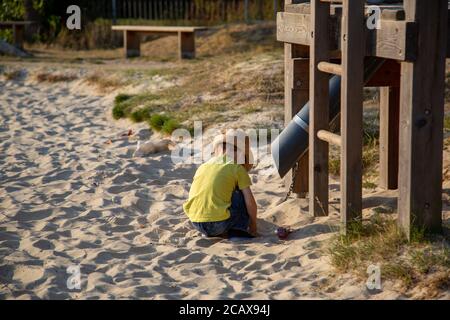 A small boy playing in a sandpit in a park during summer with a climbing frame in shot Stock Photo