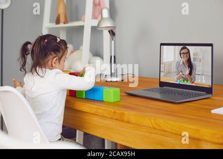 Educator teacher teaches the child online. A child does a lesson sitting at a table using a laptop remotely at home. Stock Photo