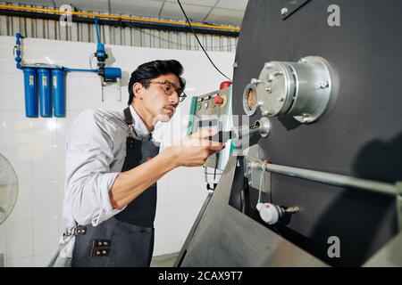 Serious Vietnamese roastery worker using probe when controlling roasting process Stock Photo