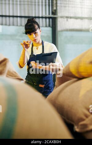 Concentrated female warehouse worker with clipboard in hands counting sacks and filling document Stock Photo