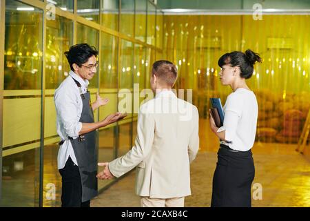 Smiling mixed-race worker in apron welcoming investors to roastery Stock Photo