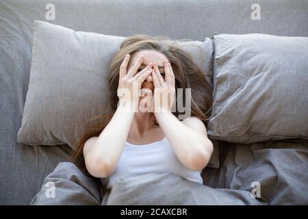 Top view of pretty girl lying on bed and covering her face with hands Stock Photo