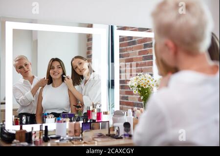 team of professional caucasian makeup artists working with young model. two make-up artist doing make-up in two hands and talk Stock Photo