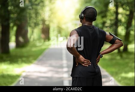African guy sportsman rubbing his back, exercising at park Stock Photo