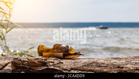A close-up of shards of a broken glass bottle against the background of water and a passing boat after people resting on the river bank. Garbage pollu Stock Photo