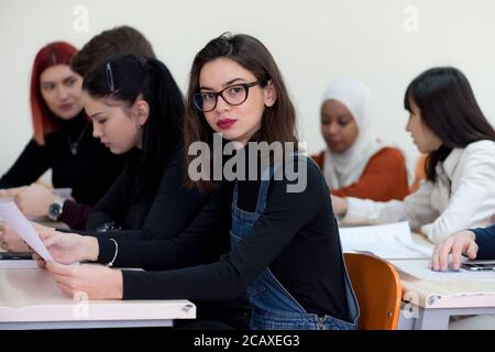 Exams Preparation. Group Of Multi-Ethnic Students Studying Together inside classroom while helping each other. Female student smiling into camera. Stock Photo