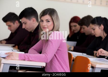 Exams Preparation. Group Of Multi-Ethnic Students Studying Together inside classroom while helping each other. Female student smiling into camera. Stock Photo