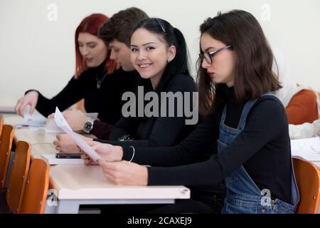 Exams Preparation. Group Of Multi-Ethnic Students Studying Together inside classroom while helping each other. Female student smiling into camera. Stock Photo