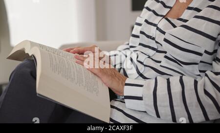 Senior woman reading a book in the comfort of her home. Close up no face. High quality photo Stock Photo