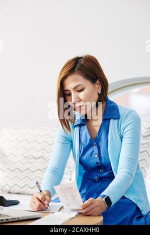 Serious businesswoman checking bills and taking notes in textbook Stock Photo