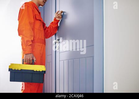 Handyman in bright orange uniform holding toolbox knocking on door of client Stock Photo