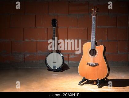 Acoustic guitar and a blurry banjo the background  against a raw brick wall in the rehearsal room of a garage band, copy space, selected focus, narrow Stock Photo