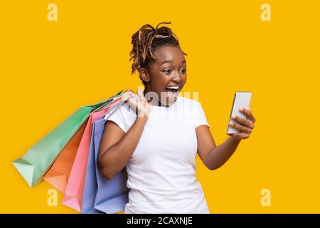 Surprised african girl with shopping bags looking at smartphone screen Stock Photo