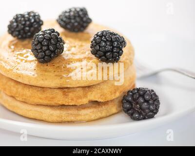 A stack of three pancakes on white plate and table, viewed from the side, garnished with blackberries, and a fork silverwear, selective focus, cropped Stock Photo