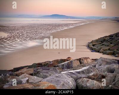 Idyllic empty beach seashore scene at sunrise, showing rocks, sand, sea and hills in the background Stock Photo