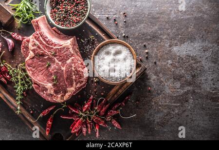Raw beef steak on wooden cutting board with salt spices chili peppers thyme and rosemary Stock Photo