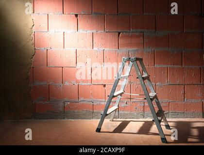 Step ladder in front of a brick wall from Porotherm style blocks partly plastered with clay in a construction site of a new building, copy space Stock Photo