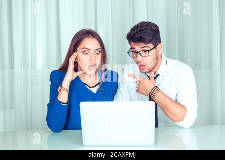 Shocking news. Two surprised couple coworkers colleagues man and woman shocked looking at laptop sitting at office table in living room at home. Freel Stock Photo