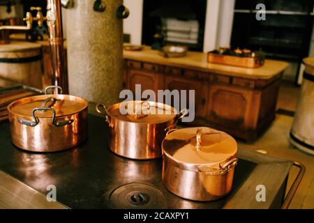 Three copper pots on the stove against the background of a long wooden table in a vintage dining room. Stock Photo