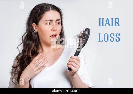 Hair loss. A terrified brunette woman holds a comb in her hands, with a bunch of hair that has fallen out. White background. Concept of baldness and h Stock Photo