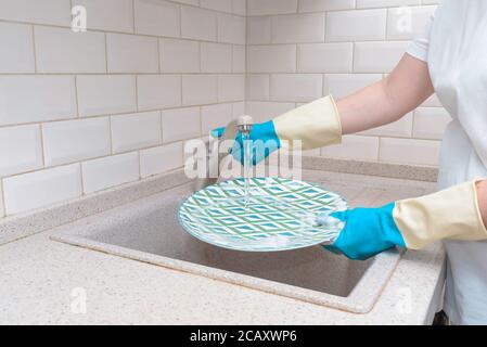 Woman washes dishes. Washing dishes - hands with gloves in kitchen, housework Stock Photo
