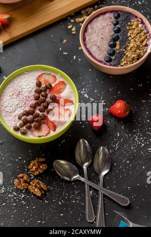 delicious dairy dessert with berries and nuts. two bowls with yoghurt and teaspoons on the black table Stock Photo