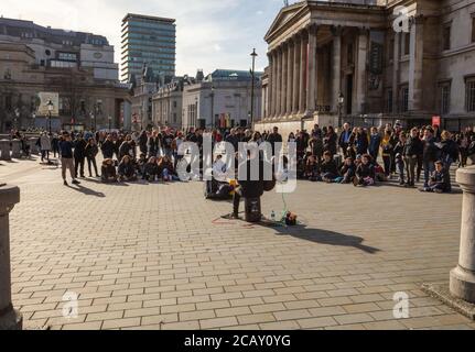 Audience looking at and listening to a guitar playing singer busker on Trafalgar Square. Stock Photo