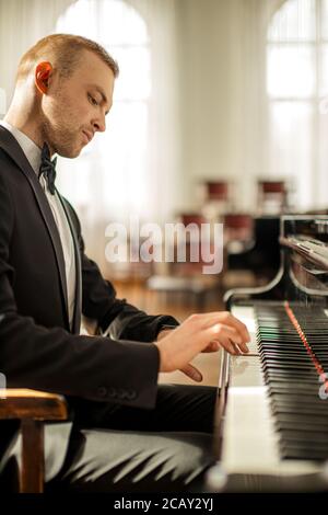 young talented male in formal suit professionally play piano. classical music performer practice playing piano before performance Stock Photo