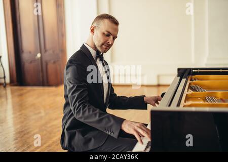 young talented male in formal suit professionally play piano. classical music performer practice playing piano before performance Stock Photo