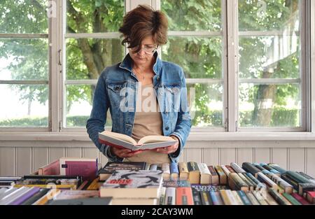 Closeup on stylish middle aged caucasian woman reading a book in old vintage bookshop Stock Photo