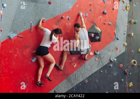 A couple of sporty people doing challengin activity. Confident female is searching where to put her foot. Strong male pulling himself upwards. Stock Photo
