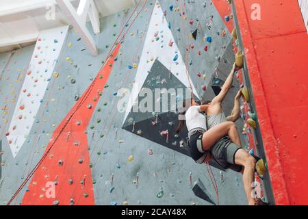 ambitious sportsman and woman moving up on steep rock, climbing on artificial wall.copy space . low angle view Stock Photo
