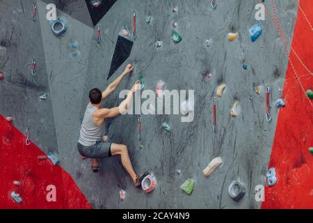 Adult man moving on the climbing wall. Powerful man trying to reach the top of the climbing wall. Stock Photo