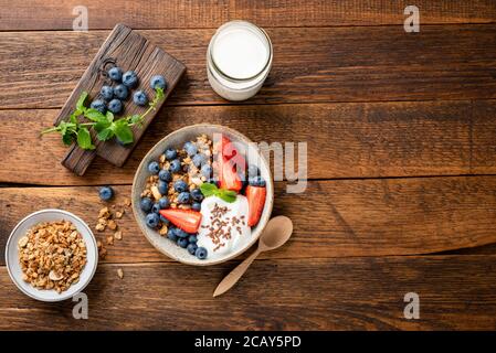 Oat granola with greek yogurt and summer berries in a bowl. Top view on a rustic wooden table background, copy space. Nutrition, healthy eating concep