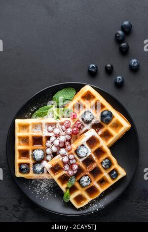 Sweet belgian waffles with berries decorated with icing sugar on a black stone background. Top view Stock Photo