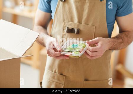 Close up of unrecognizable man wearing apron packaging individual food portions, food delivery service worker , copy space