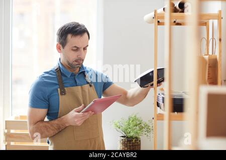 Waist up portrait of mature man wearing apron using digital table while doing inventory in food delivery service, copy space Stock Photo