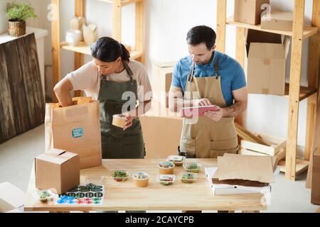 High angle view at two workers wearing aprons packaging orders at wooden table in food delivery service, copy space Stock Photo