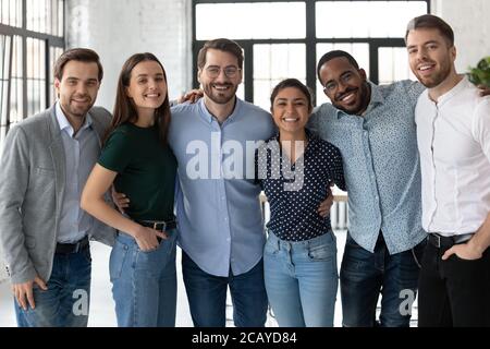 Smiling diverse business people hugging, standing in modern office Stock Photo
