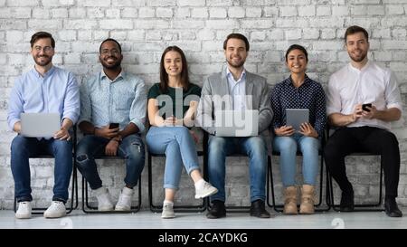 Portrait smiling diverse candidates sitting on chairs in row Stock Photo