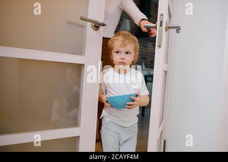 little caucasian boy, child stay near the door at home holding blue dish in hands, sweet child Stock Photo