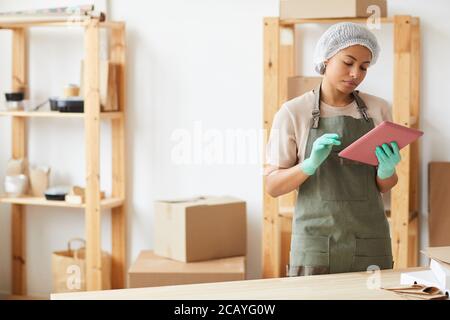 Waist up portrait of female worker using digital tablet while working in kitchen at food delivery service, copy space Stock Photo