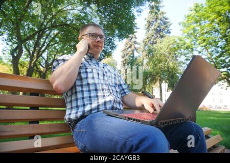 Guy sitting with laptop and talking on the phone in the park Stock Photo