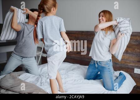 caucasian family consisted of mother father and kid girl having fun together playing with pillows at home on bed Stock Photo