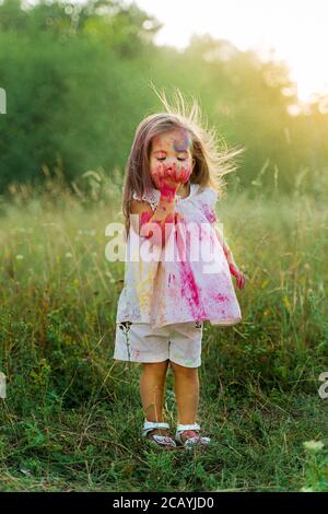 the little girl was covered in holi paint. a girl in a green clearing. hair up Stock Photo