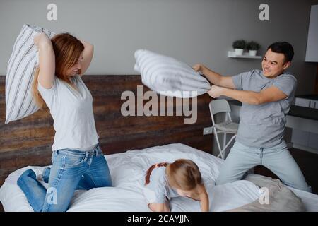 happy caucasian family, mother father and child girl fight play with pillows on bed, cheerful family concept Stock Photo