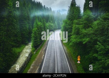 Aerial view of road in beautiful green forest in low clouds Stock Photo